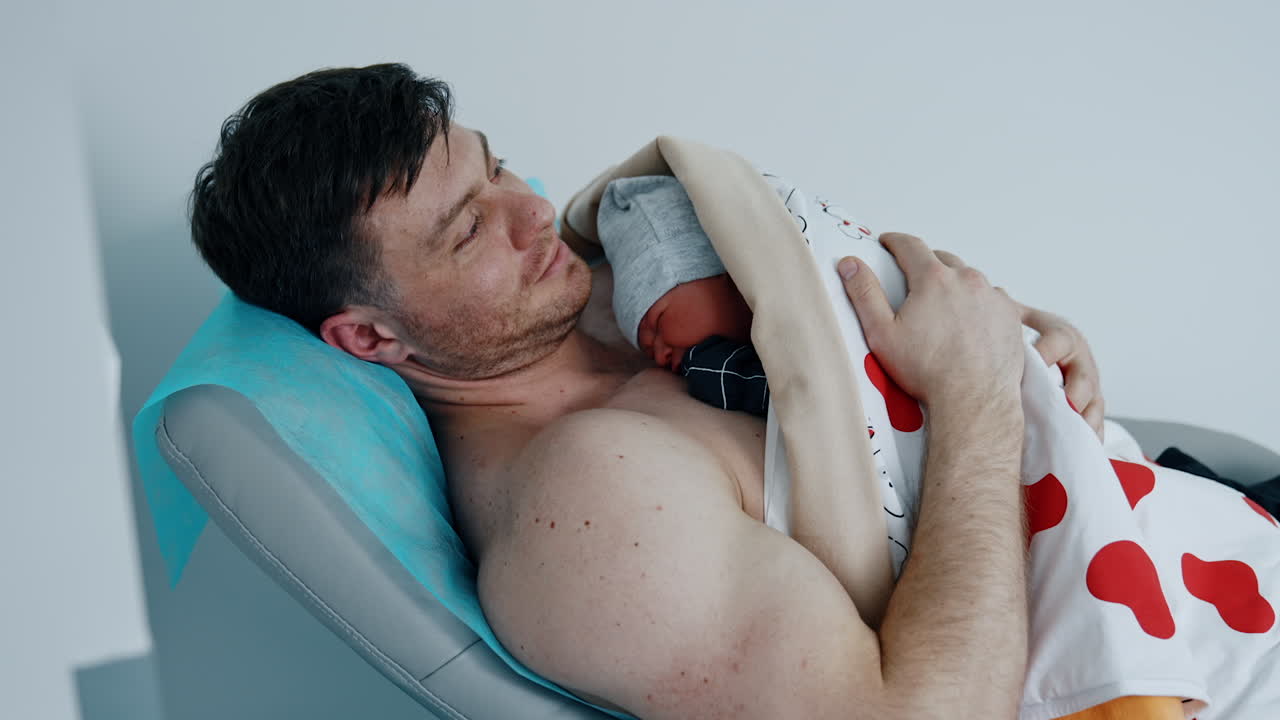 Father is happy to hold and caressing his newborn baby. The child is laid on the dad's chest right after birth.