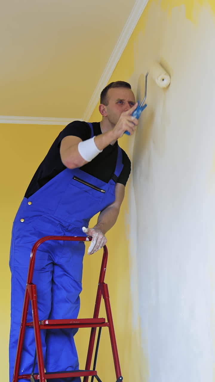 Young man in new apartment renovating room. Handsome painter working with brush roller renewing home. Vertical video