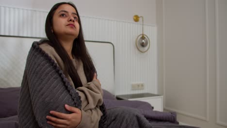 Sad-woman-with-a-cold-in-a-brown-jacket-and-a-dark-gray-stove-takes-pills-during-her-illness-Sitting-on-the-bed-in-a-modern-apartment-in-the-bedroom