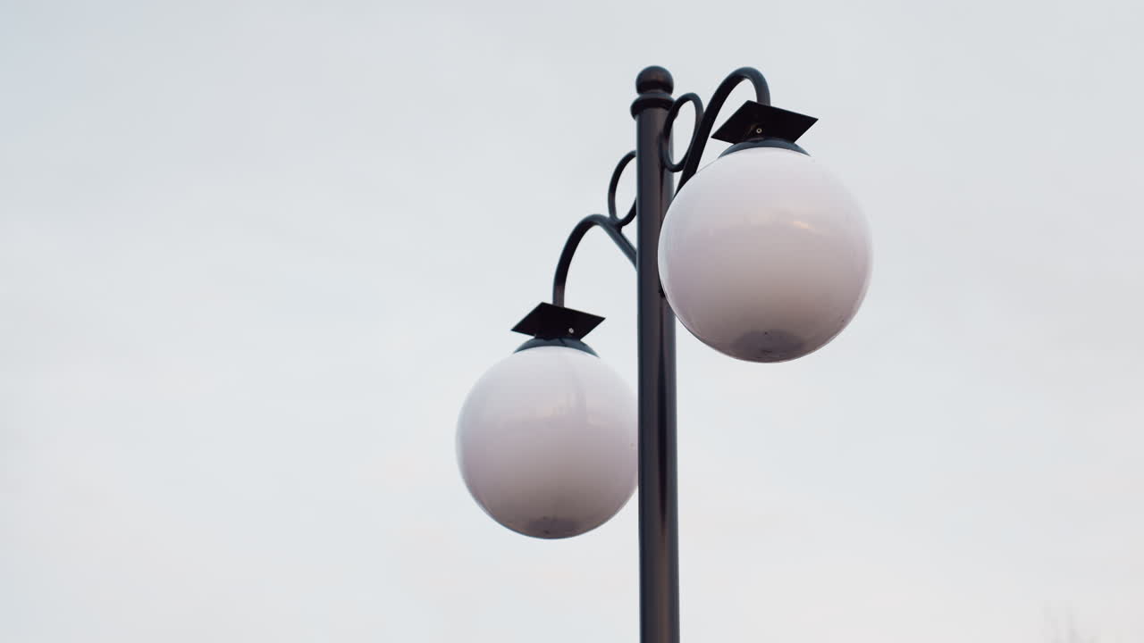 Close up view of tall lamp poles with round white bulbs standing against soft pale sky in winter park, emphasizing minimal composition, modern outdoor lighting, and tranquil seasonal ambiance