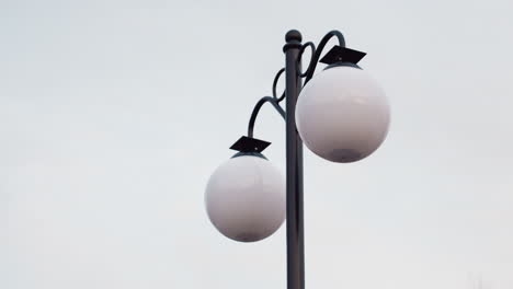 close up view of tall lamp poles with round white bulbs standing against soft pale sky in winter park, emphasizing minimal composition, modern outdoor lighting, and tranquil seasonal ambiance
