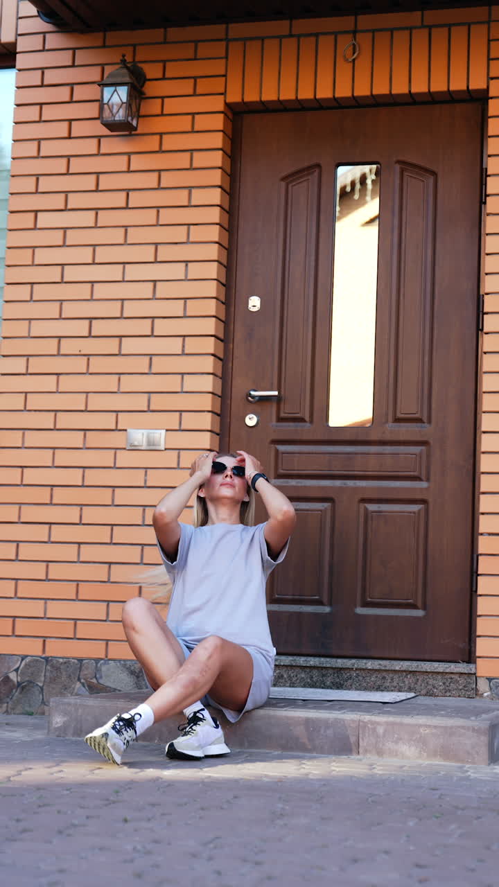 Woman sitting by a brown door outside. A young woman with long hair sits casually on steps beside a brown door, enjoying a moment of relaxation in sunlight