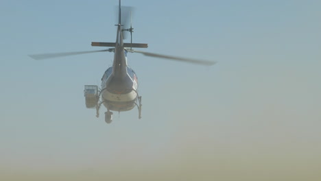 a helicopter taking flight in the desert with cars driving past and dust cloud