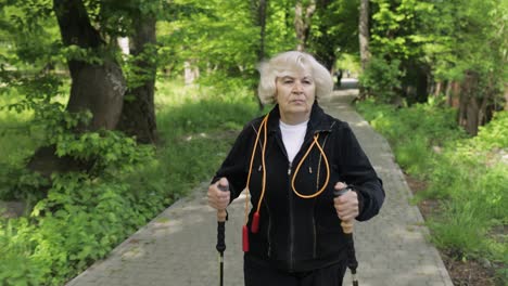 Aktive-ältere-Frau-Trainiert-Nordic-Walking-Mit-Ski-Trekkingstöcken-Im-Park