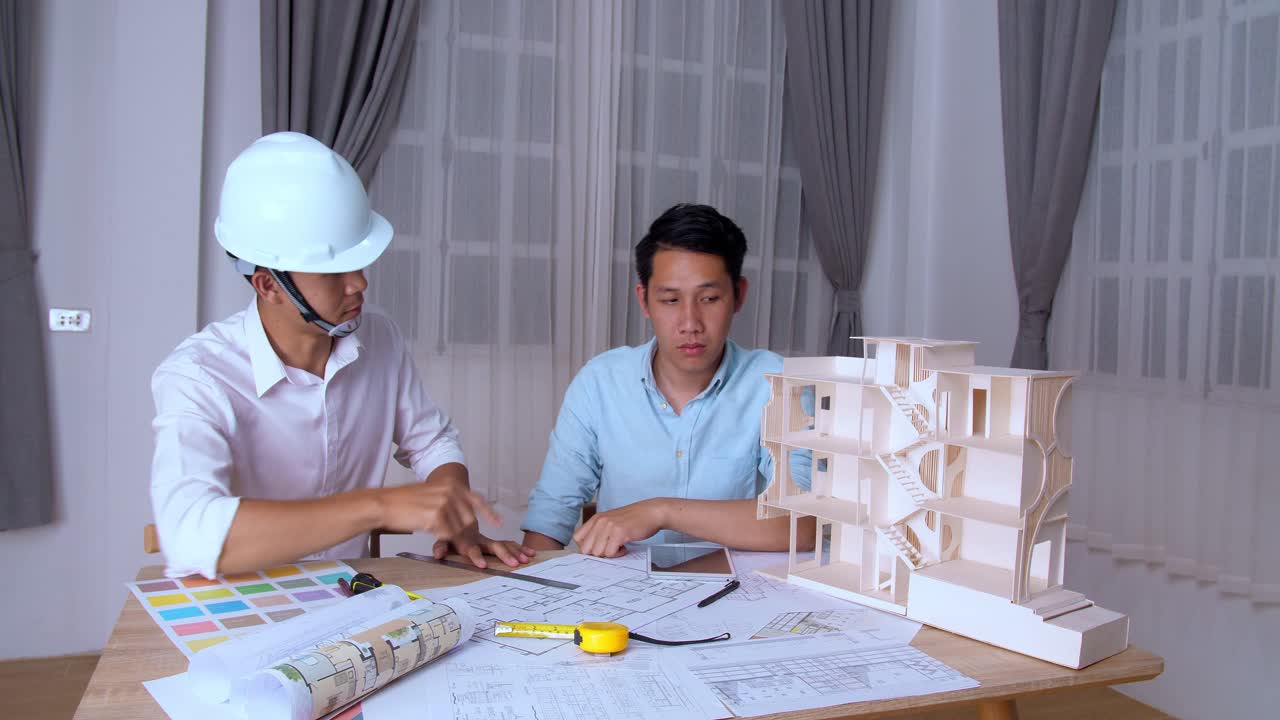 Two Asian Male Architects In Office Discussing Construction Project