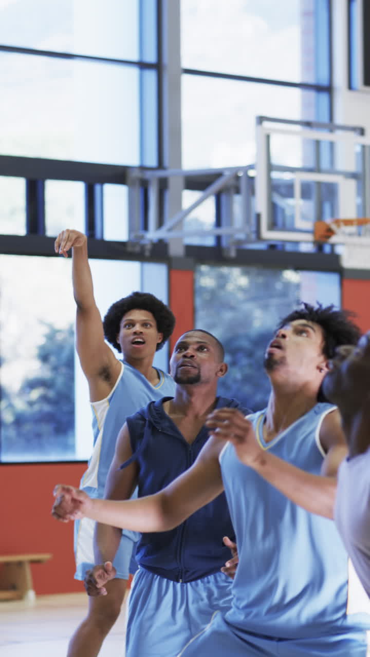 Vertical video of diverse male basketball team training in indoor court, in slow motion