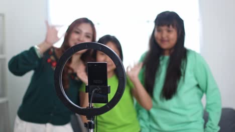 happy asian mother and daughters using a mobile phone and a ring light for recording video together at home