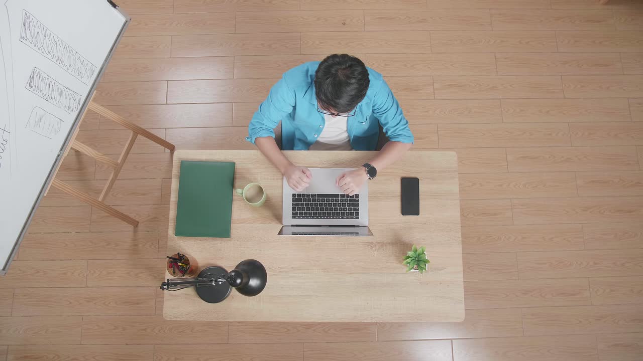 스마트 폰 에 노트북에서 타이핑하는 성공을 축하하는 남자의 상단 뷰 집에서 화이트 보드 에 나무 책상에 앉아있는 동안