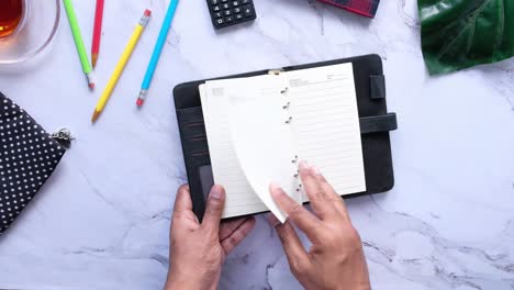 hands opening a black notebook on a marble desk