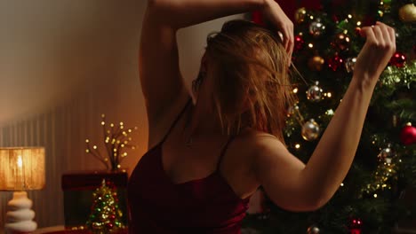 una mujer atractiva vestida con una falda de terciopelo juega sensualmente con su cabello y sonríe hacia la cámara en una habitación decorada con navidad