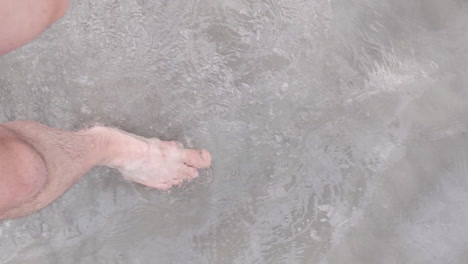 man barefoot in shorts walks in the clear shallow beach water of the salt lake in utah