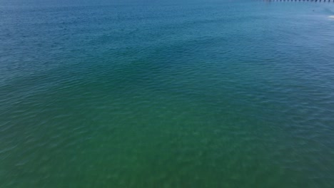 tilt up revealing the oceanside pier above green clear sea water