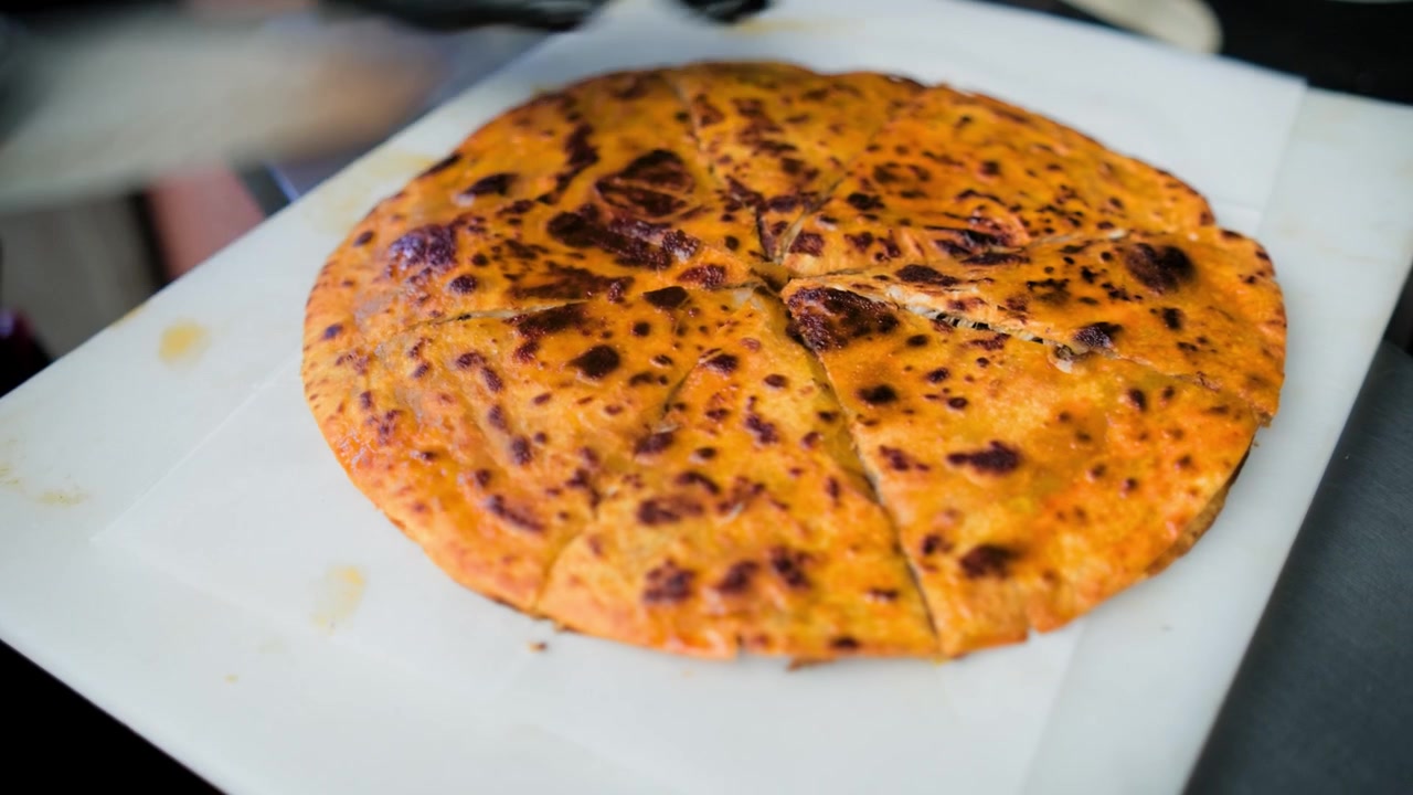 Riprese di cucina commerciale che mostrano una birria pizza affettata per l'asporto durante la preparazione di una gustosa birria pizza su una piastra