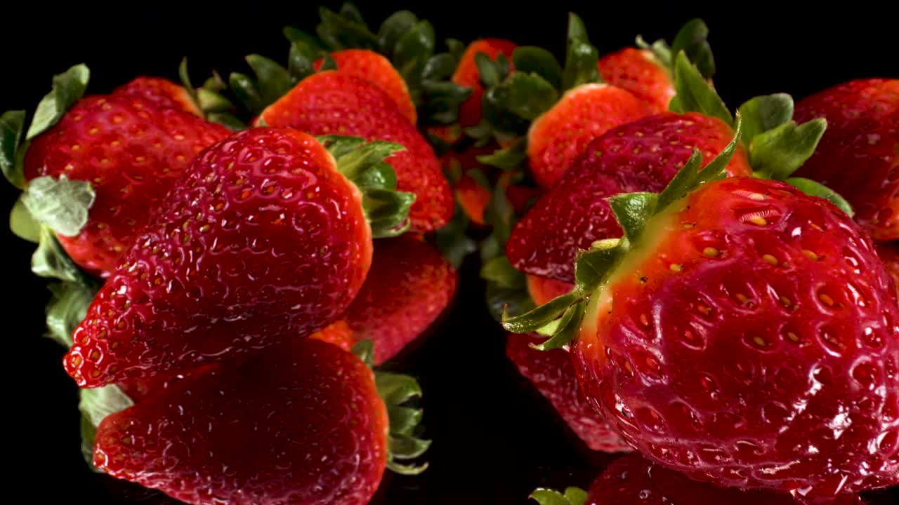 macro vista passando attraverso fragole rosse su sfondo di vetro nero riflettente, elegante colpo 4k di frutta fresca sana