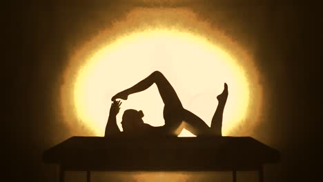 silhouette of a contortionist woman doing acrobatics on a table