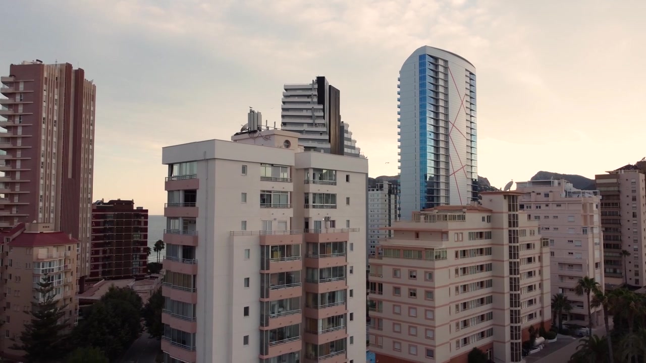 Clipe de drone sobre a cidade costeira de Calpe na Espanha, revelando arranha-céus e hotéis durante o pôr do sol.