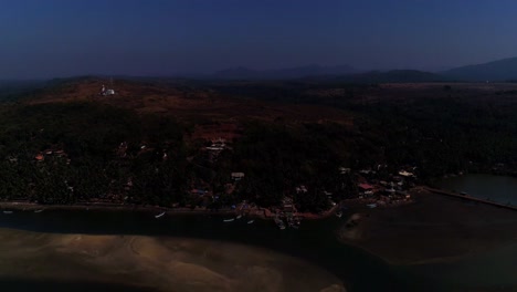 dron que avanza hacia un pueblo de pescadores ubicado en un remanso con colinas onduladas con un templo y una casa de luz
