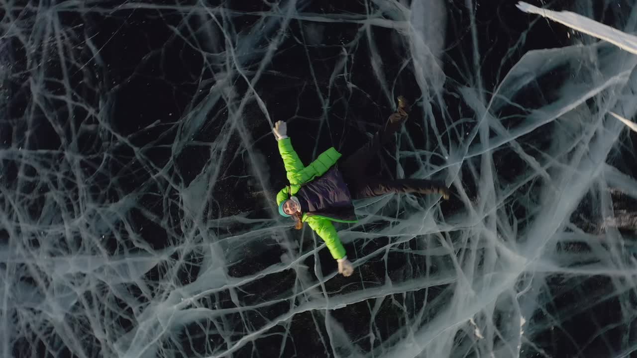 una chica yace en el hielo en invierno con ropa cálida y agita sus brazos y piernas