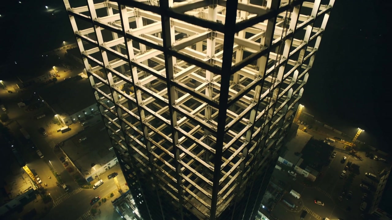 Moving drone revealing steel high-rise, approaching tower exposing lit slabs highlighting structure