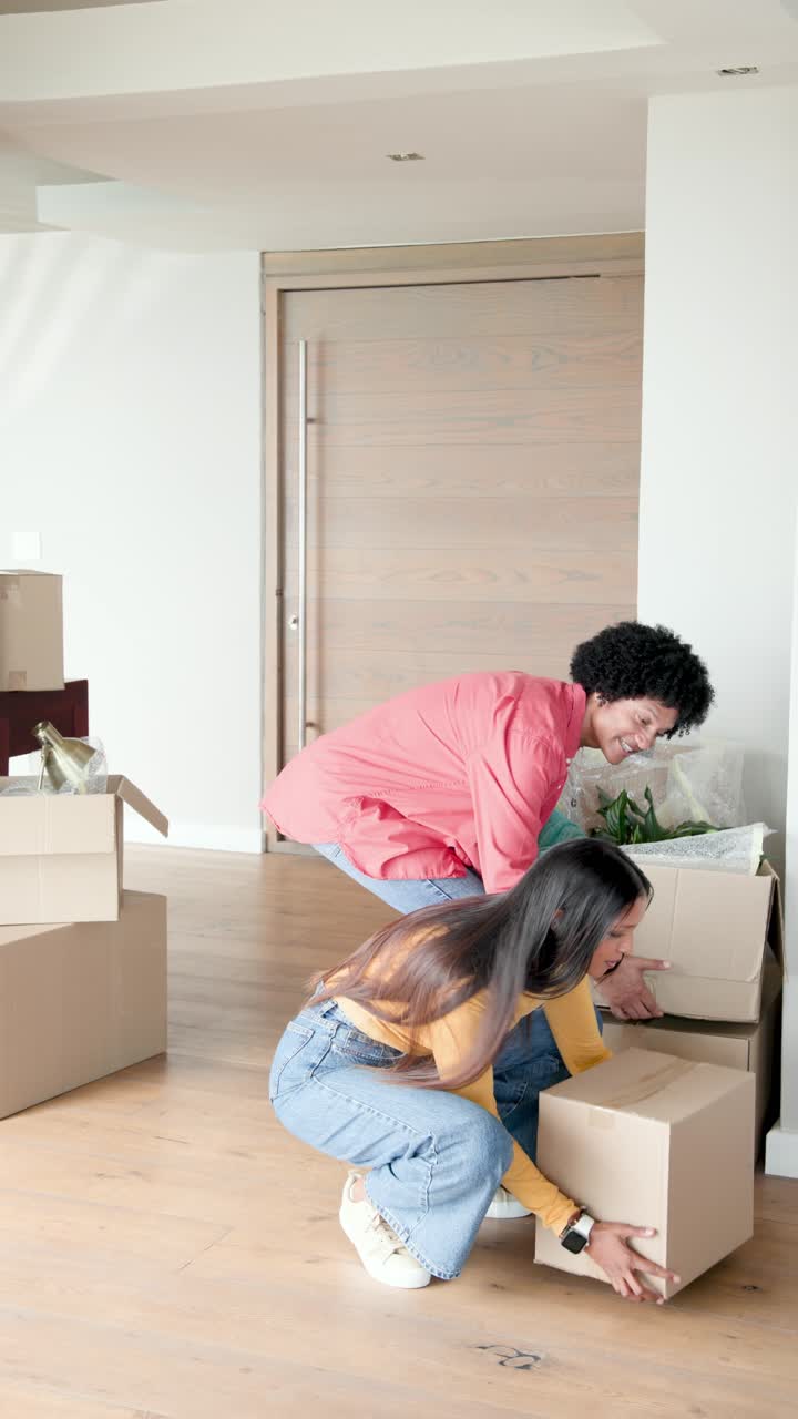 Vertical video: Diverse couple stepping through wooden entry door placing boxes and unpacking items