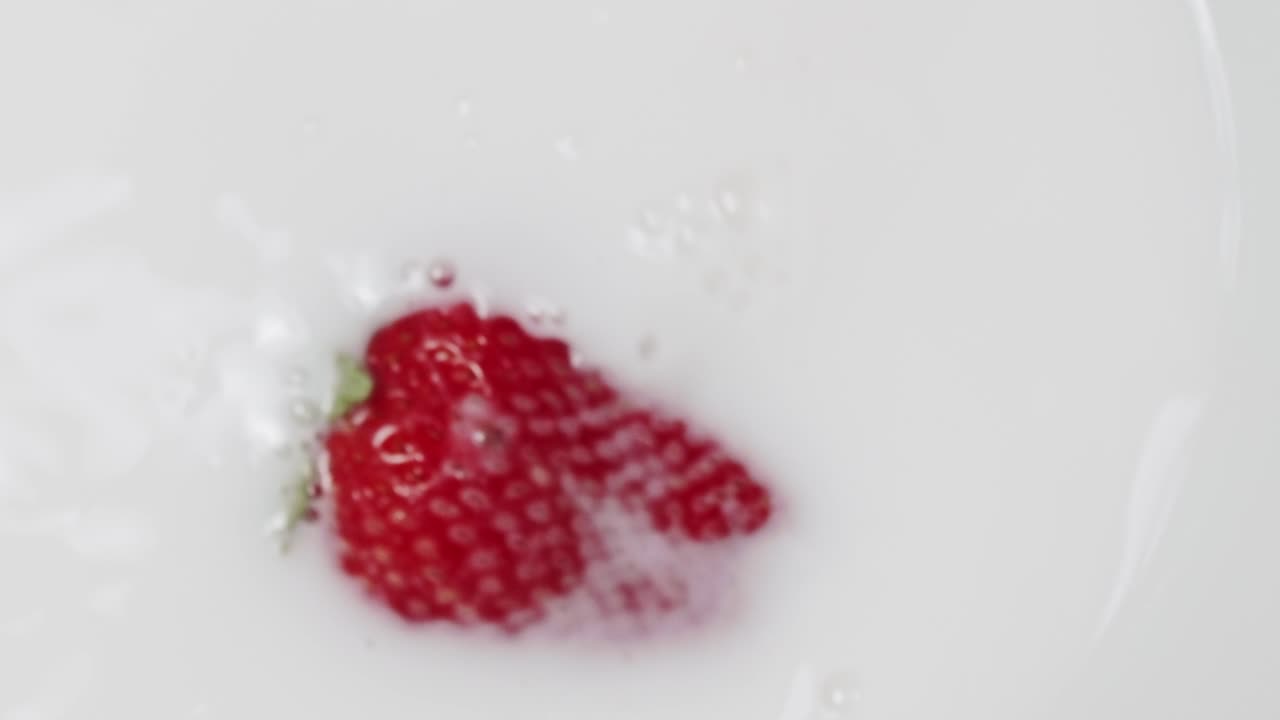 One single red strawberry splashing into white milk