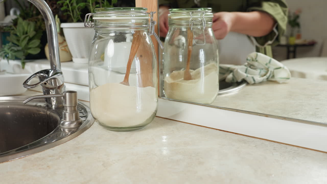 Close up of chef gently lifting egg crate from countertop with mirrored reflection in background, surrounded by kitchen jars filled with flour and sugar