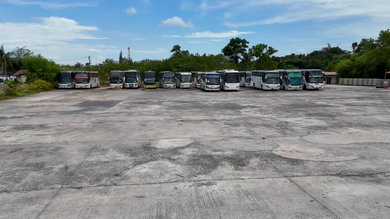Aerial footage captures a deserted lot with rusting buses in Phuket, Thailand, under bright daylight, conveying a sense of abandonment