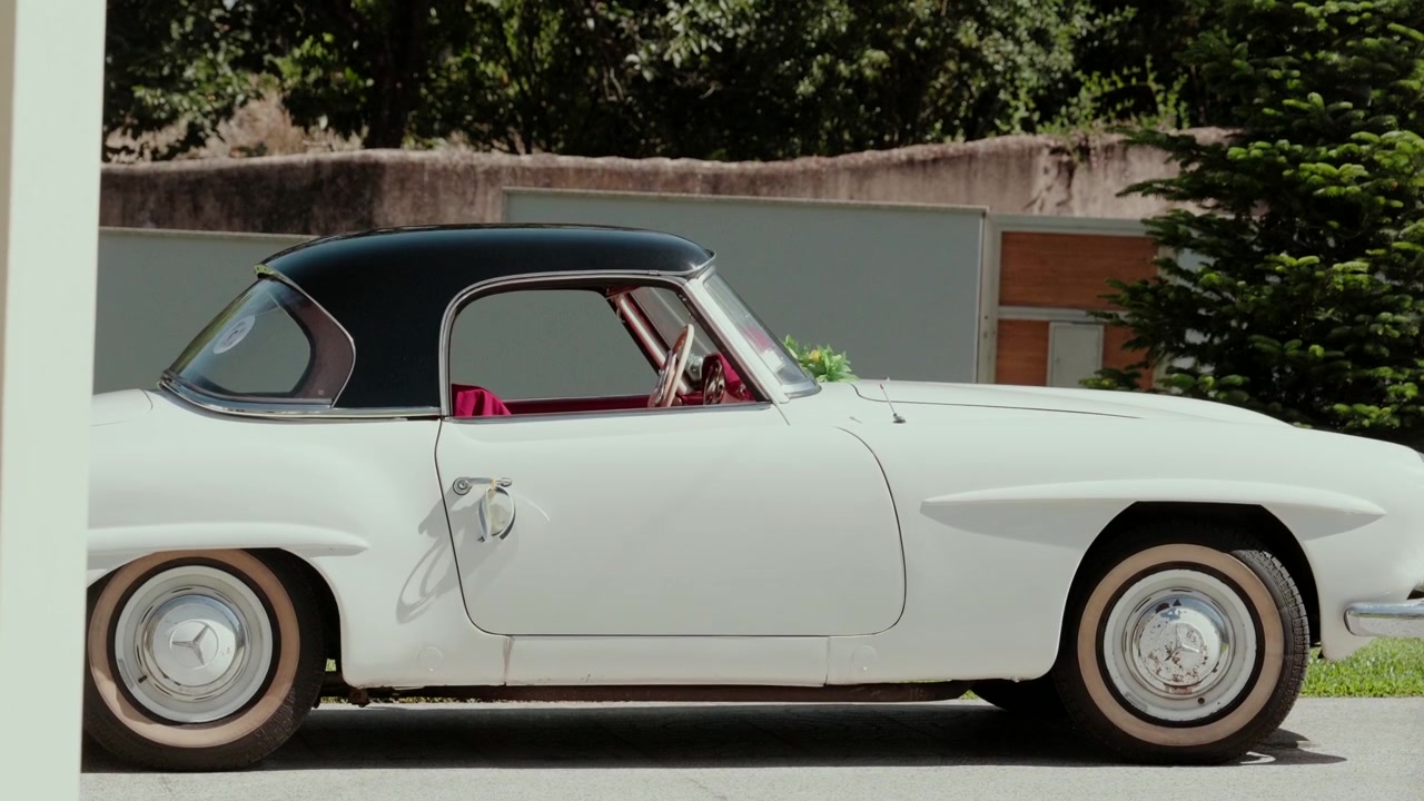 Roadster Mercedes bianca classica con hardtop nero e interni in pelle rossa parcheggiata all'aperto