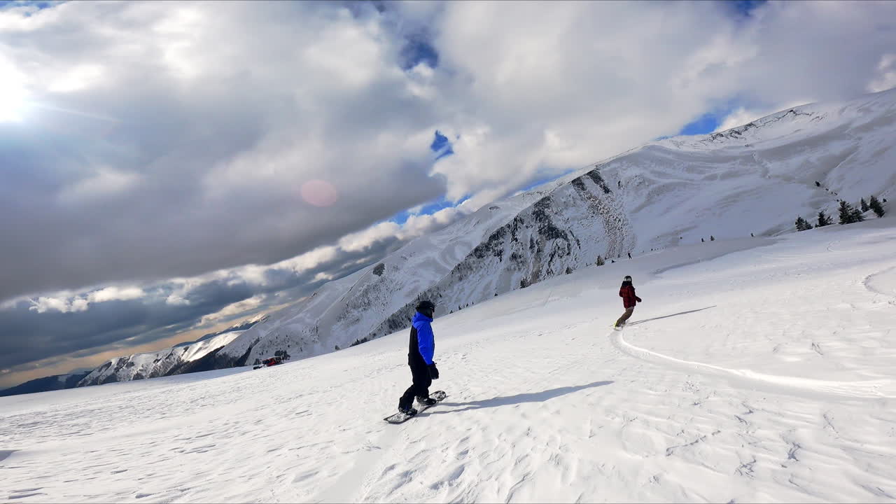 Snowboarders go down the hill by the snow shining in the sun. Dramatic cloudscape at backdrop.