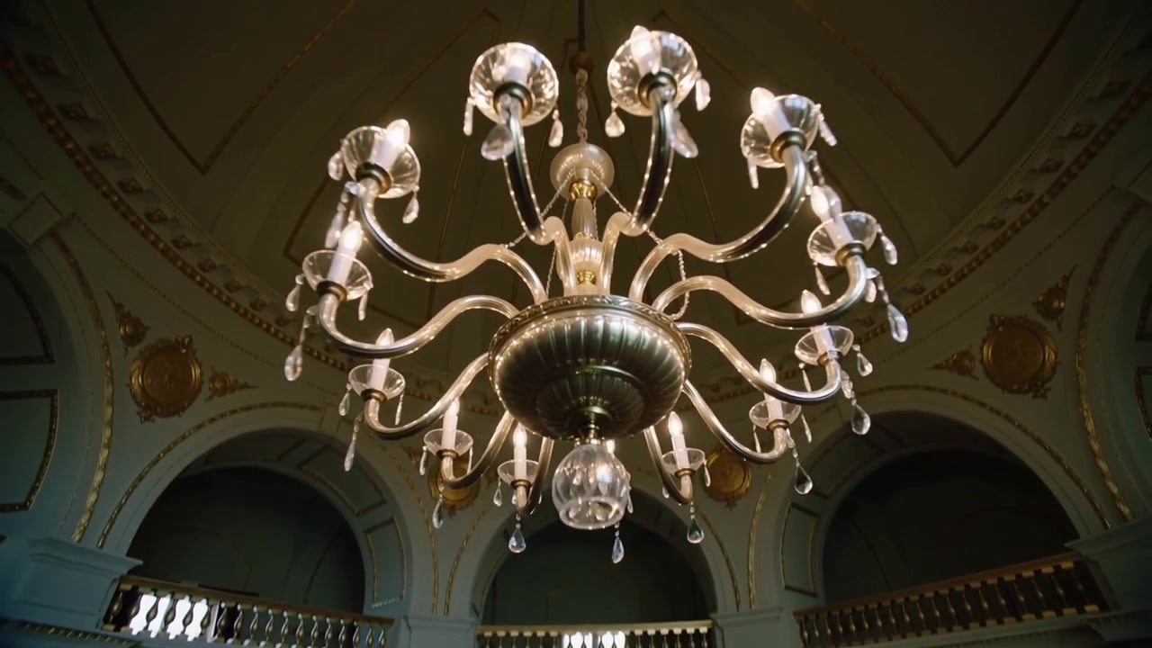 Panoramica a comando, telecamera che gira attorno a un lampadario di cristallo in una rotonda a cupola, rivelando archi dorati.