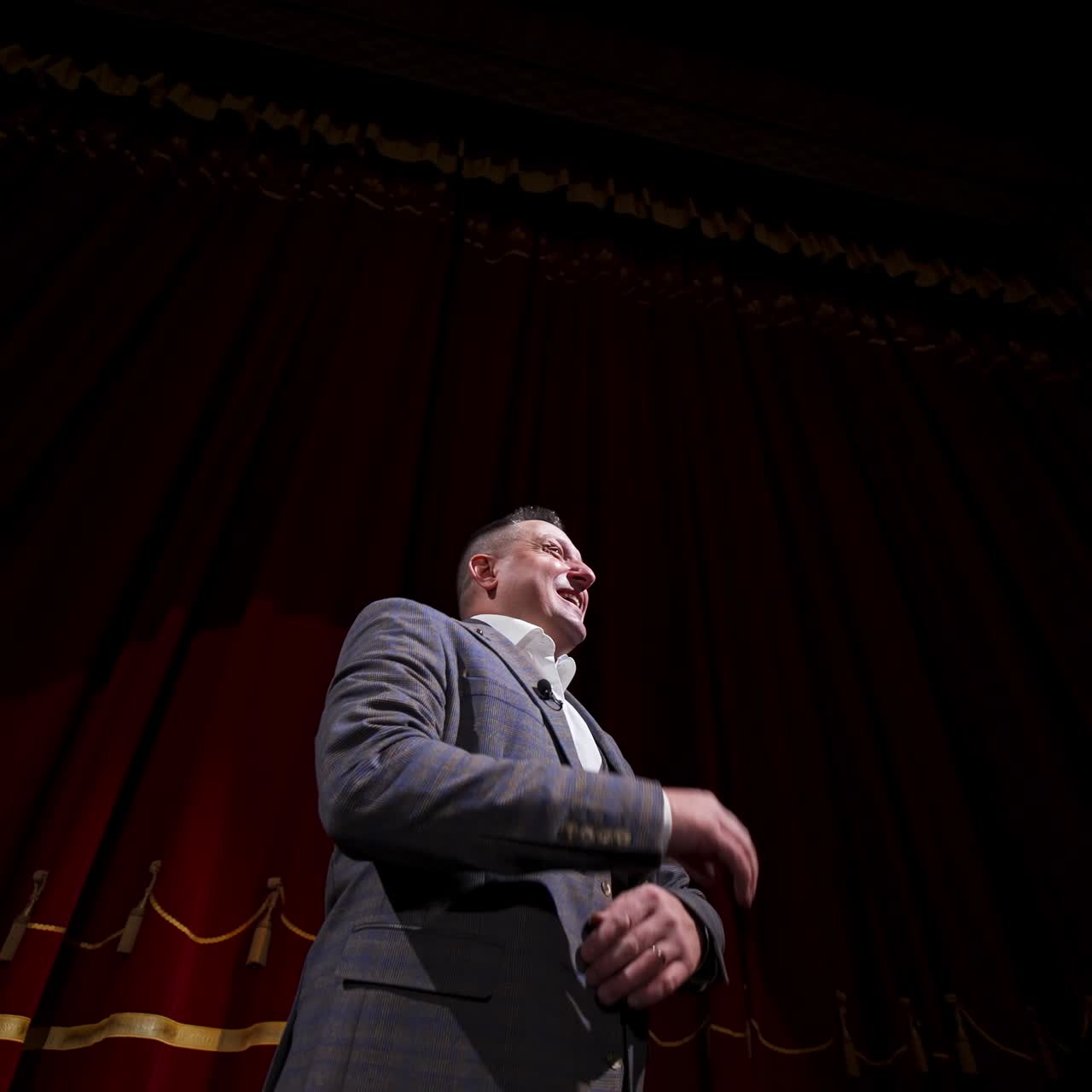 Theatrical man on stage. Performer in a suit moving on stage on red curtains background. Professional actor performing in theater. View from below