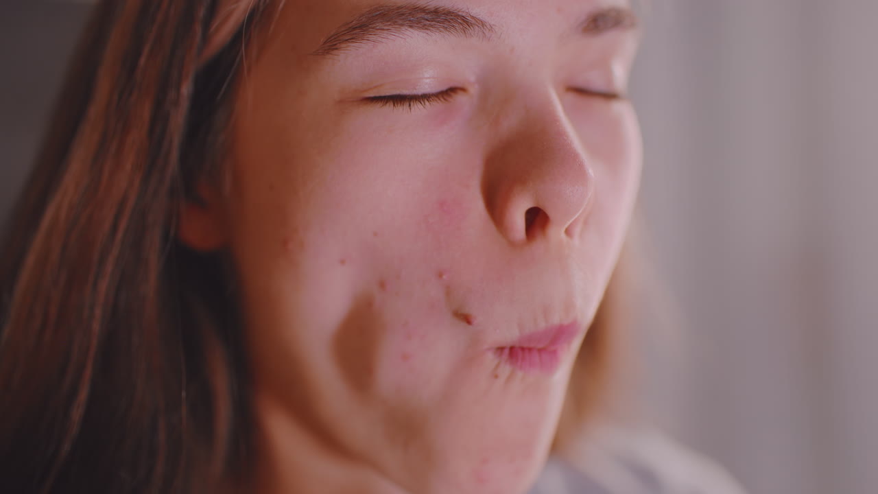 Close up of lady enjoying snack with cucumber slice layered on bread, gentle bite showing relaxed mood, warm indoor light illuminating face and hands, capturing natural moment of casual eating