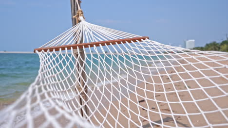 Hamaca-De-Cuerda-De-Algodón-Colgada-En-La-Playa-Cerca-Del-Mar-En-Un-Día-Soleado,-Una-Sola-Persona-Ancha-Con-Gruesas-Barras-Esparcidoras-De-Madera-Dura-Hamaca