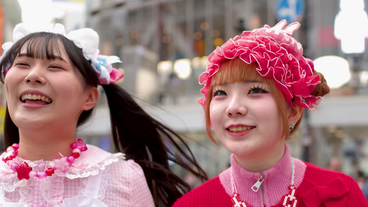 Due giovani donne che indossano abiti in stile decora rosa vivace sorridono e ridono a Shibuya