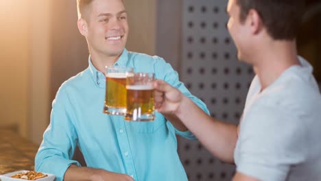 Two-happy-caucasian-male-friends-holding-pints-of-beer,-making-a-toast-at-bar