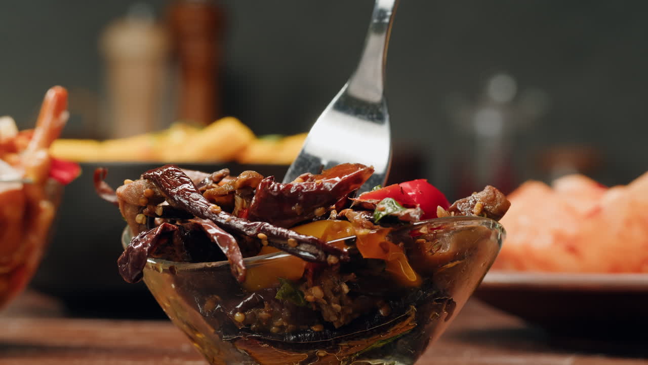 Taking a little bit of fermented eggplants with spices and mustard by fork close-up. Preservation of vegetables in glass jars. Fermentation preserved aubergine with greens.