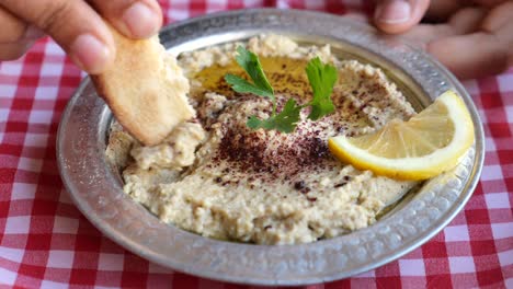 hand dipping pita bread into hummus with lemon and parsley