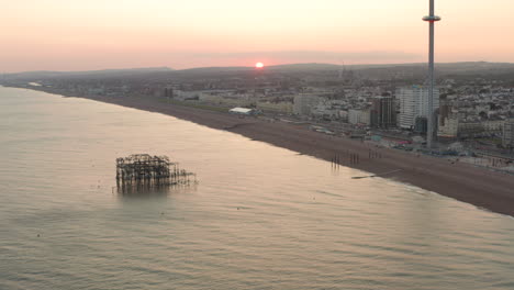 Toma-Aérea-Circular-Del-Sol-Poniéndose-Detrás-Del-Viejo-Muelle-De-Brighton