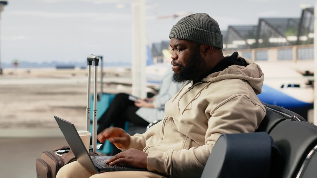 Uomo afroamericano lavora al portatile e beve caffè in aeroporto