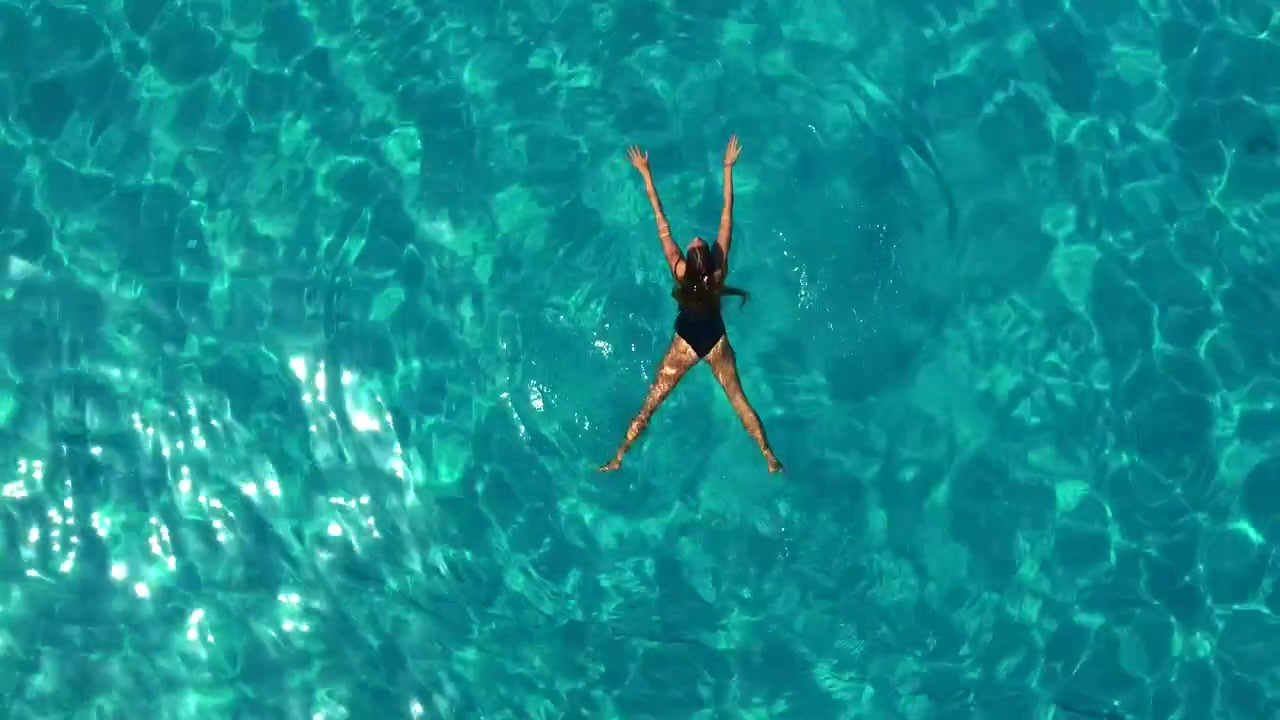 Vista aerea dall'alto di una donna che galleggia e nuota nelle acque limpide color turchese del Mar Ionio ad Antipaxos, Grecia