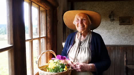 a happy elderly woman in a straw hat holding a basket of flowers by a rustic window