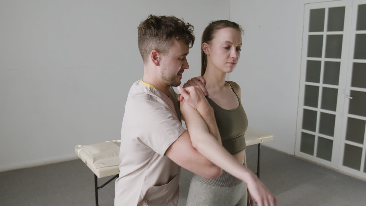 A physical therapist performs a shoulder rehabilitation exercise on a female patient.