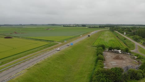 Toma-Aérea-De-Tráfico-En-Una-Carretera-A-Través-De-Tierras-Agrícolas-En-La-Península-De-Walcheren-En-Zelanda,-Los-Países-Bajos-En-Un-Día-Nublado-De-Verano