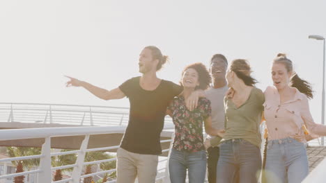 group of young friends outdoors walking across bridge together against flaring sun