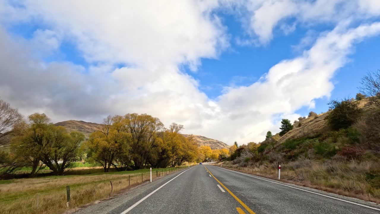 A serene drive through Wanaka's countryside, showcasing vibrant autumn foliage under a bright blue sky