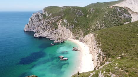 Praia-Ribeira-do-Cavalo-Beach-near-Sesimbra,-Alentejo,-Portugal---Aerial-Drone-View-Flying-along-the-Rocky-Coastline-to-the-Hidden-Sandy-Beach-and-Turquoise-Sea