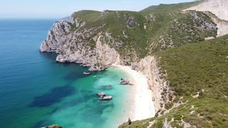 praia ribeira do cavalo beach cerca de sesimbra, alentejo, portugal - vista aérea de drones volando a lo largo de la costa rocosa hasta la playa de arena escondida y el mar turquesa
