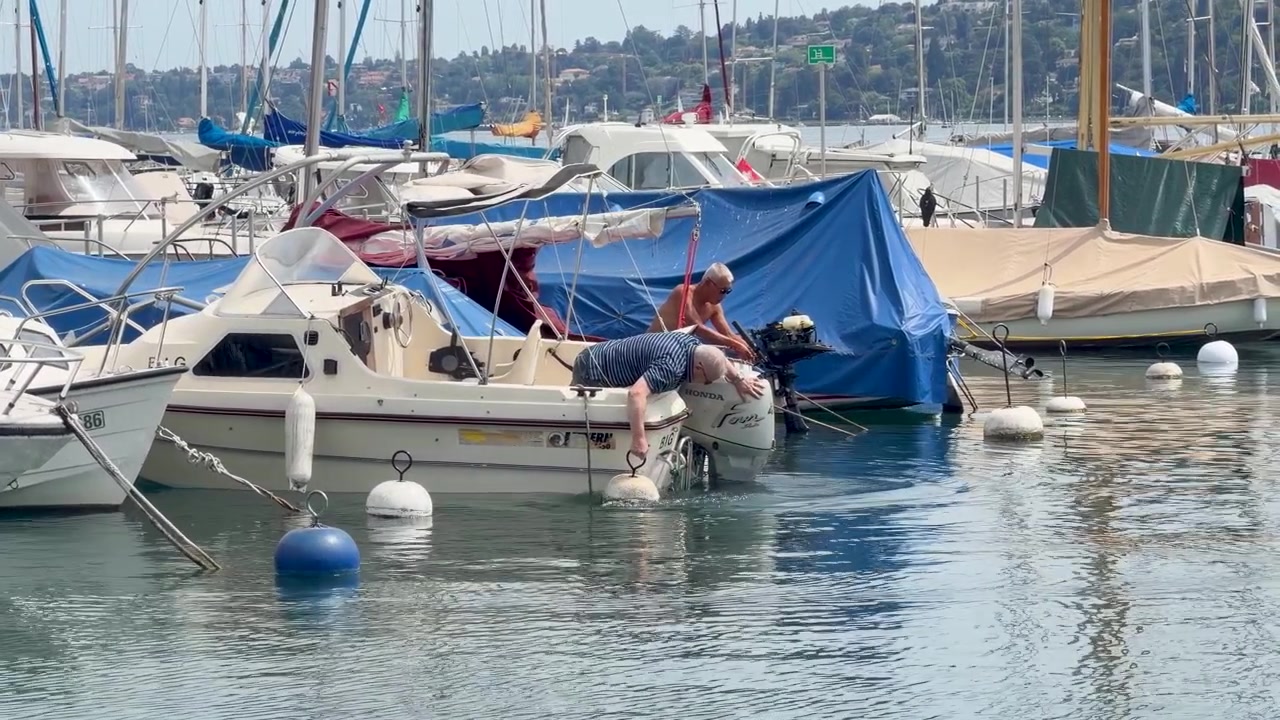 Due uomini anziani ispezionano e riparano un motore di motoscafo in un molo soleggiato di un porto turistico sul lago