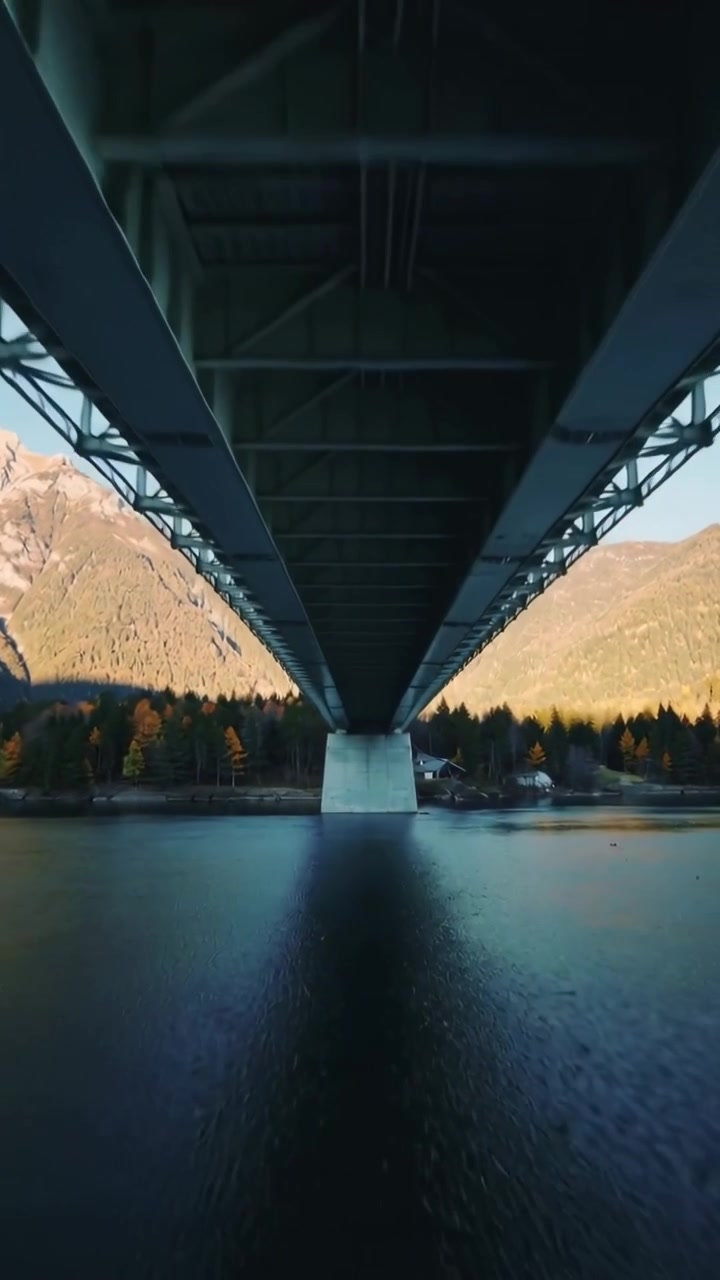 Vertical video: Pulling camera revealing bridge underside over water, center pier and valley slopes