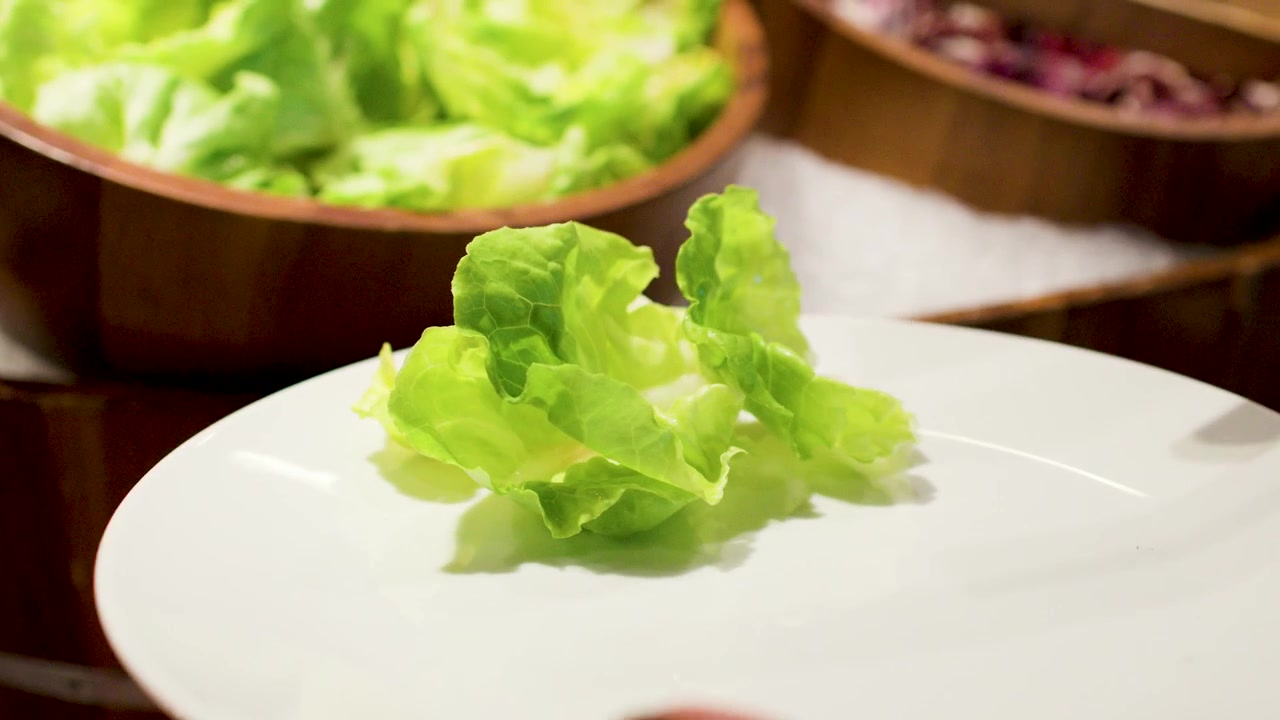 手部特寫鏡頭，正在自助餐桌上將新鮮綠色生菜放上碟子。